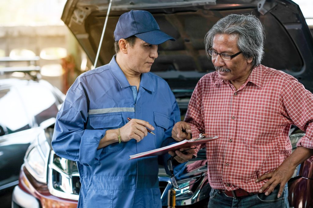 Asian automotive mechanic with blue uniform explain about the lists of problem of car
